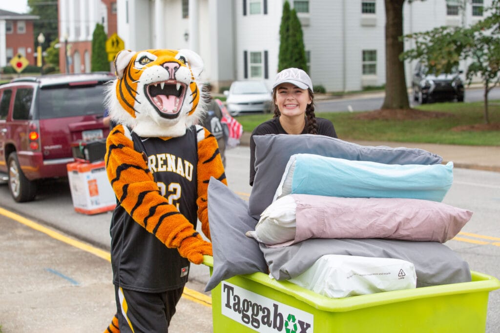 HJ the tiger and a volleyball player help move a student's belongings in a cart