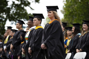 graduates in black robes and mortar boards stand in a line