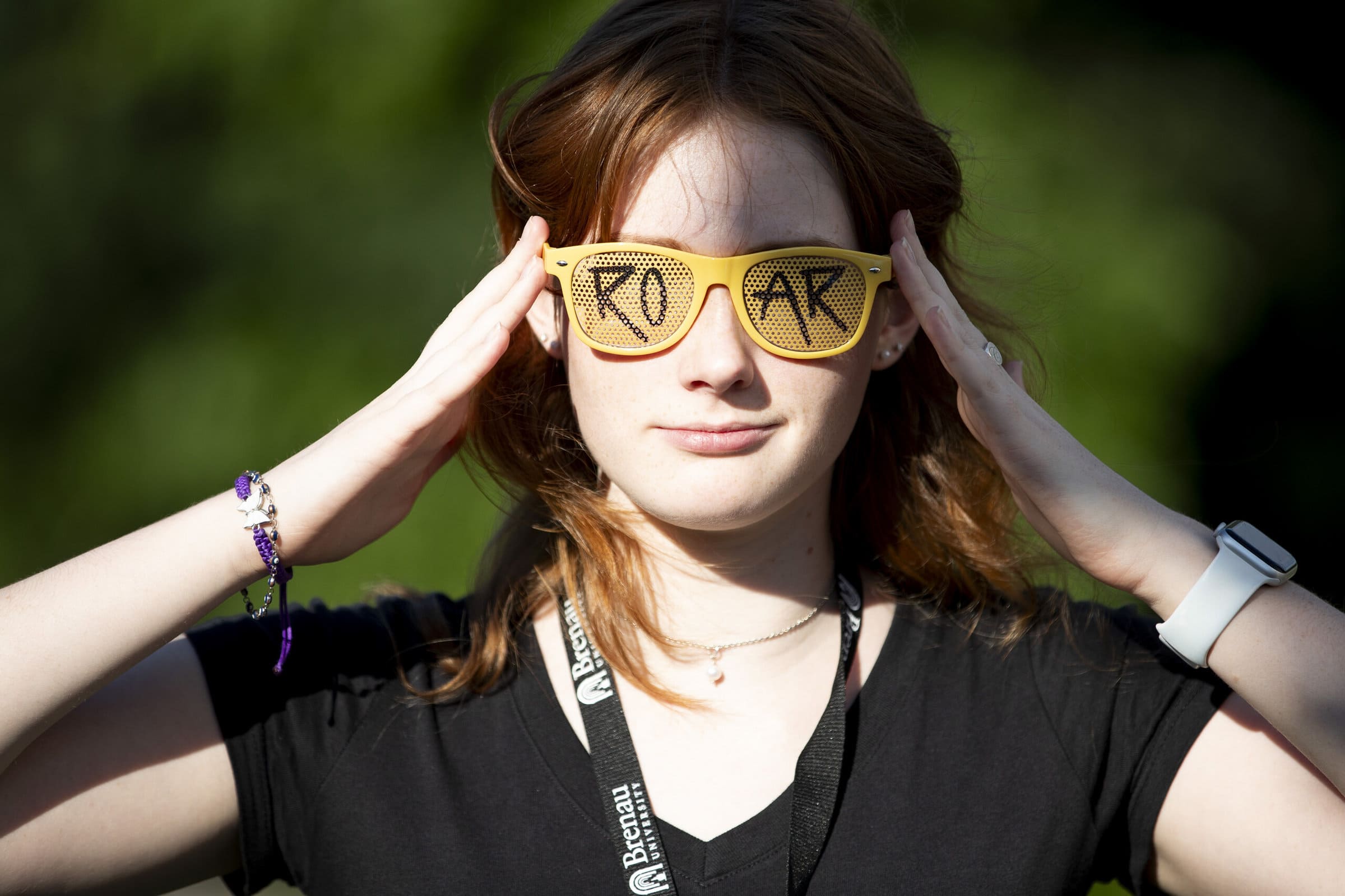 A redheaded woman wears a pair of yellow sunglasses that read 