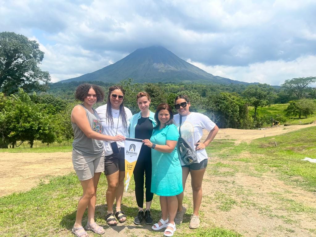 Brenau students and faculty hold a school pennant in front of a mountain in Costa Rica.