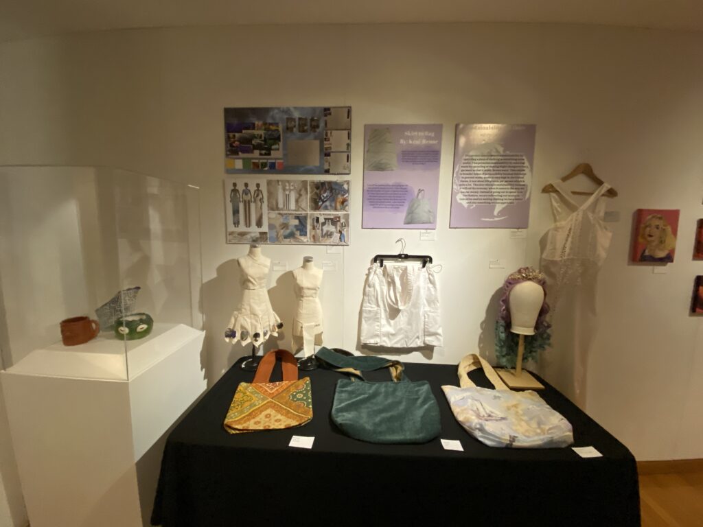 Ceramic art in a display case next to student made clothing and tote bags on display.